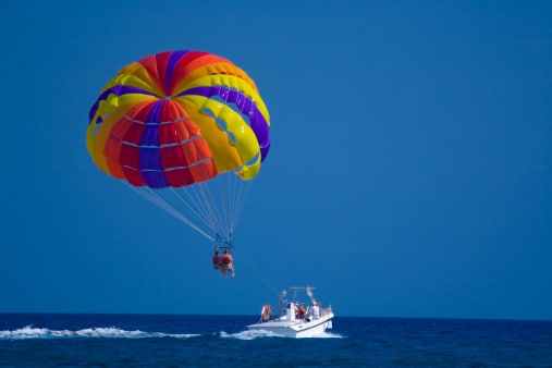a colorful parasail in the air being pulled by a boat