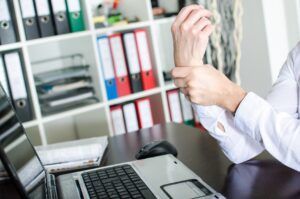 work injury lawyer Chicago, IL with a man holding his wrist in pain sitting in front of a laptop