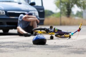 Person sitting next to wrecked bike in front of a car before calling a Bicycle Accident Lawyer Springfield, IL