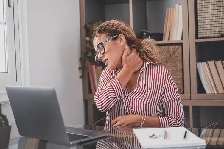 Disability for fibromyalgia, Image of woman touching neck in pain at desk