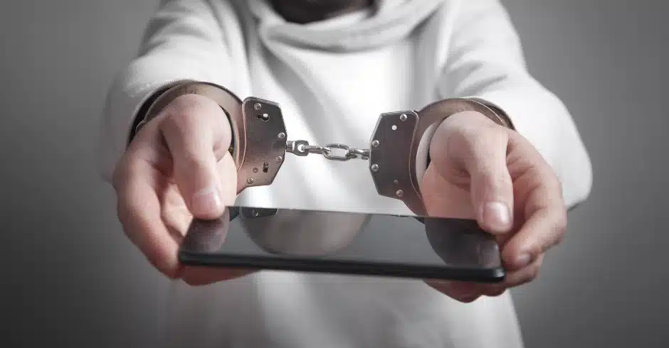 Social media addiction, image of a person holding out a cell phone with hand cuffs on.