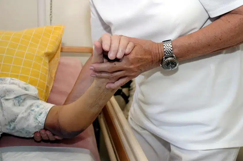 Bedsores in nursing homes, image of nurse holding elderly person's hand in bed. 